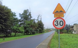 Znak ostrzegający przed szkodami górniczymi oraz ograniczenie prędkości, w tle droga, domy, drzewa